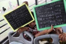 Dua anak laki-laki menunjukkan papan tulis kecinya di dalam bus "Harapan" yang dijadikan ruang kelas bergerak mereka, yang diparkir di daerah kumuh, dataran banjir sungai Yamuna, New Delhi, India 9 Agustus 2021. (REUTERS)
