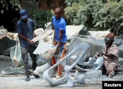 Zimbabwean sculptor Dominic Benhura carries a finished piece at his studio in Harare, Zimbabwe, March 2, 2020. (REUTERS/Philimon Bulawayo)