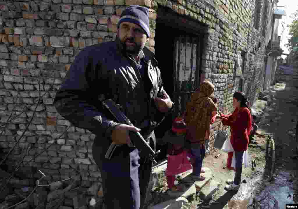 A policeman stands guard as Neila gives polio vaccine drops to a child at a Christian colony slum in Islamabad, Pakistan, December 20, 2012.