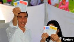 Jakarta governor and presidential candidate from the Indonesian Democratic Party-Struggle (PDI-P) party, Joko Widodo, and his wife Iriana show their ballot papers during voting in the parliamentary elections in Jakarta, April 9, 2014.