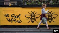 A woman passes a street-art graffiti mural, created following the May 22 terror attack at the Manchester Arena, featuring bees, which are synonymous with Manchester as a symbol of the city's industrial heritage, in Stevenson Square, Manchester.