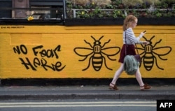 A woman passes a street-art graffiti mural, created following the May 22 terror attack at the Manchester Arena, featuring bees, which are synonymous with Manchester as a symbol of the city's industrial heritage, in Stevenson Square, Manchester.