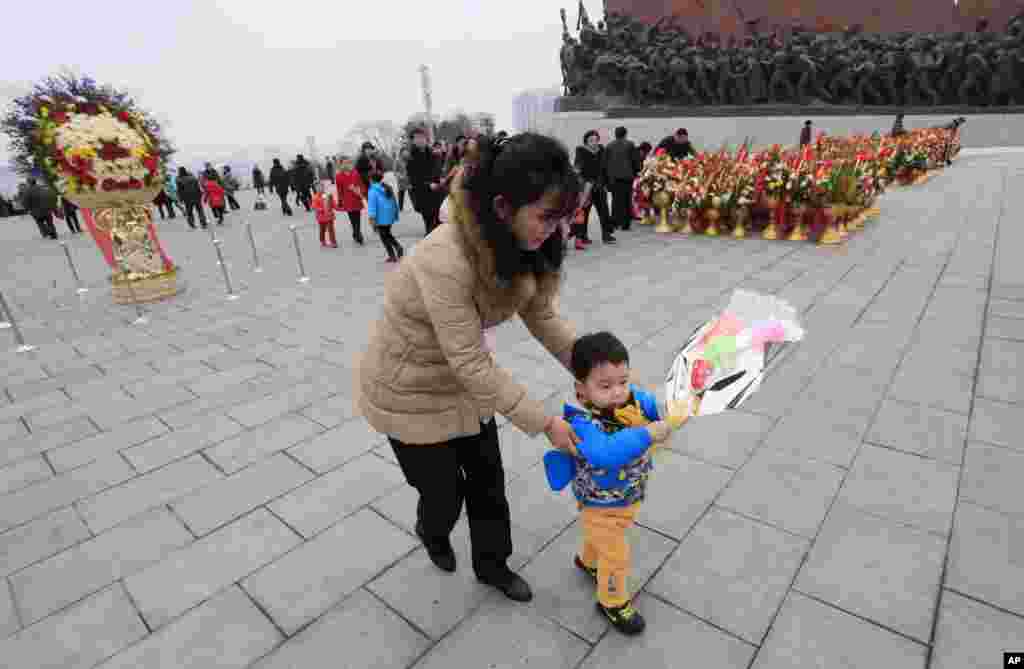 북한 김정일 국방위원장의 75돌 생일(광명성절)을 맞은 16일, 한 여성이 어린와 함께 만수대 언덕 김일성, 김정일 동상에 색종이로 만든 꽃을 바치고 있다.