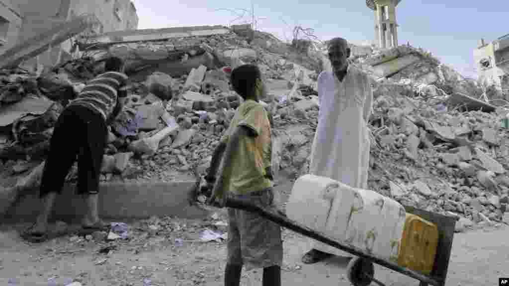 A Palestinian man talks to a boy carrying containers as they stand amid the rubble of al-Qassam mosque, hit by an Israeli airstrike Saturday, in Nusseirat refugee camp in the central Gaza Strip, Aug. 10, 2014. 