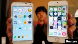 A sales assistant holding Samsung Electronics' Galaxy 5 smartphone (L) and Apple Inc's iPhone 5 smartphone (R) poses for photographs at a store in Seoul, July 16, 2014. 