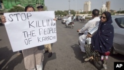 A family rides past on a motor bike as an activist of the civil society group Karachi Concerned Citizen Forum holds a placard along a road in Karachi August 20, 2011.