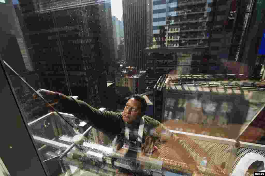 A window washer uses a squeegee to clean windows on the morning of the summer solstice in New York&#39;s Times Square.