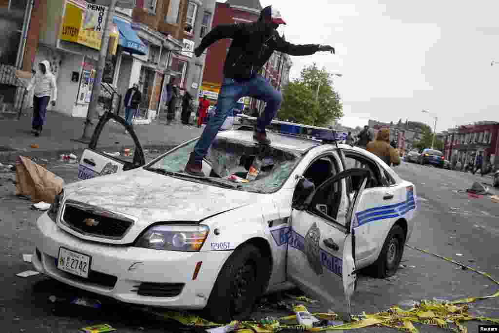 Demonstrators jump on a damaged Baltimore police department vehicle during clashes in Baltimore, Maryland, April 27, 2015. 