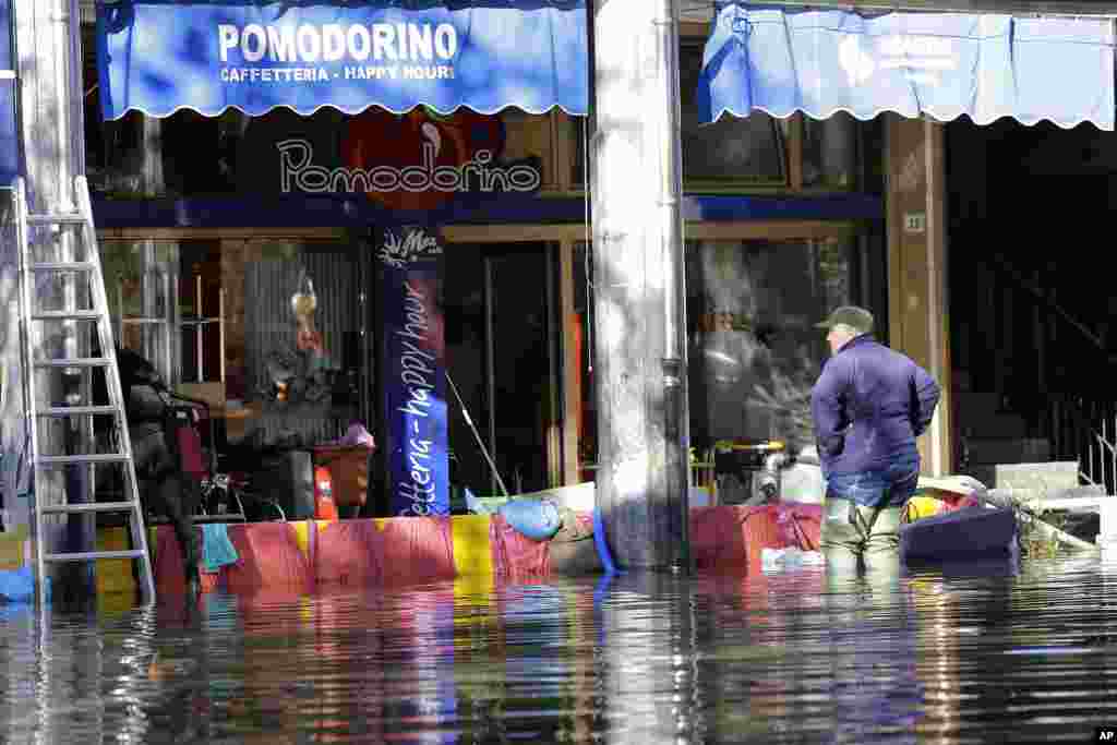 A man stops in front of a Coffee Shop along a flooded street after heavy rains hit northern Italy for the last few days in Omegna, Italy.