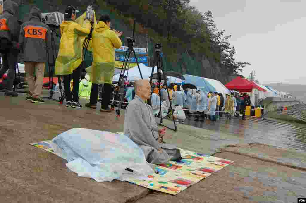 A Buddhist monk prays for the missing passengers who were on the South Korean ferry Sewol, while press and family members pass by, Jindo, April 18, 2014. (Sungmin Do/VOA)