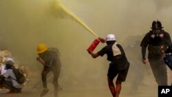 Demonstrant koristi protivpožarni aparad kako bi napravo zaklon za druge, dok pripadnici snaga bezbjednosti napreduju ka njima, u Jangonu, Mjanmar.