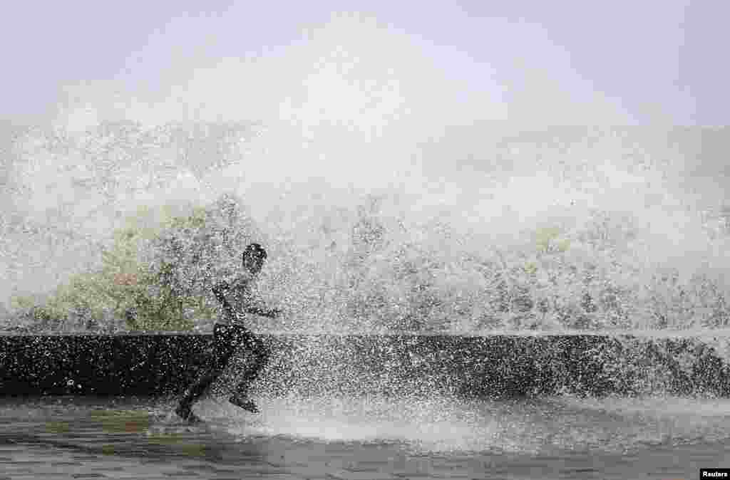 A school boy runs to get drenched in a large wave during high tide at a sea front in Mumbai.