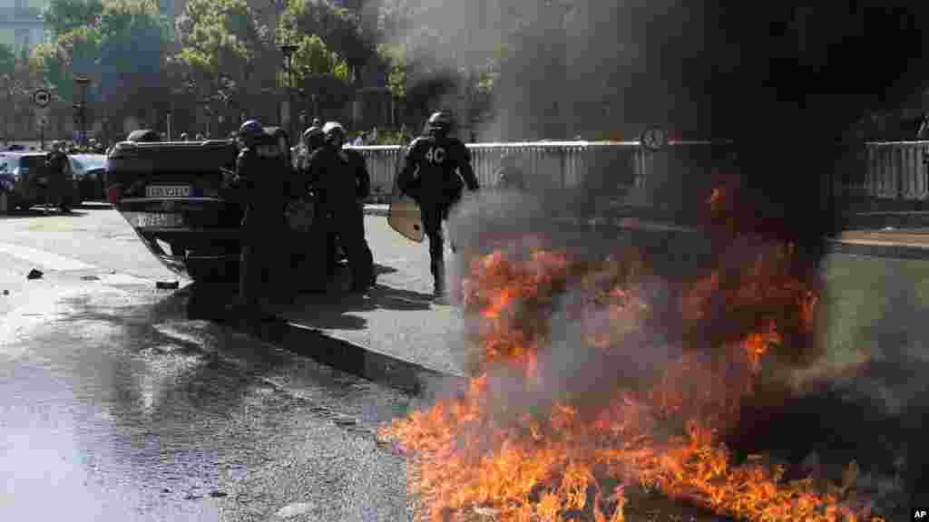 Des policiers anti-émeute se tiennent près d&rsquo;une voiture renversée et une flamme allimée par des manifestants, le 25 juin 2015, à Paris, France.