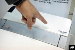 FILE - Zhong Jiye, a co-founder of Shenzhen Trump Industrial Co., points to the logo on one of his firm's high-end Trump-branded toilets at the company's offices in Shenzhen in southern China's Guangdong province, Feb. 13, 2017.