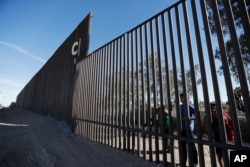 Boys look through an older section of the border structure from Mexicali, Mexico, alongside a newly constructed, taller section, left, in Calexico, California, March 5, 2018.