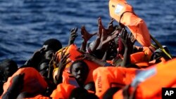 Des migrants subsahariens, mains levées, tentent d’accrocher un des gilets de sauvetage que distribuent des membres de l'ONG Proactive Open Arms, en Méditerranée, à environ 22 miles au nord de Zumarah, en Libye, 27 janvier 2017. 