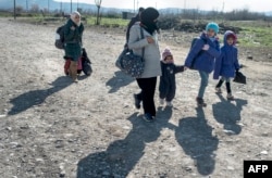 FILE - A woman and children cross the Greek-Macedonian border near the town of Gevgelija, Feb. 25, 2016.