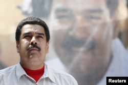 FILE - Venezuela's President Nicolas Maduro stands in front of a picture of himself during a meeting with government workers in Caracas, Nov. 20, 2015.