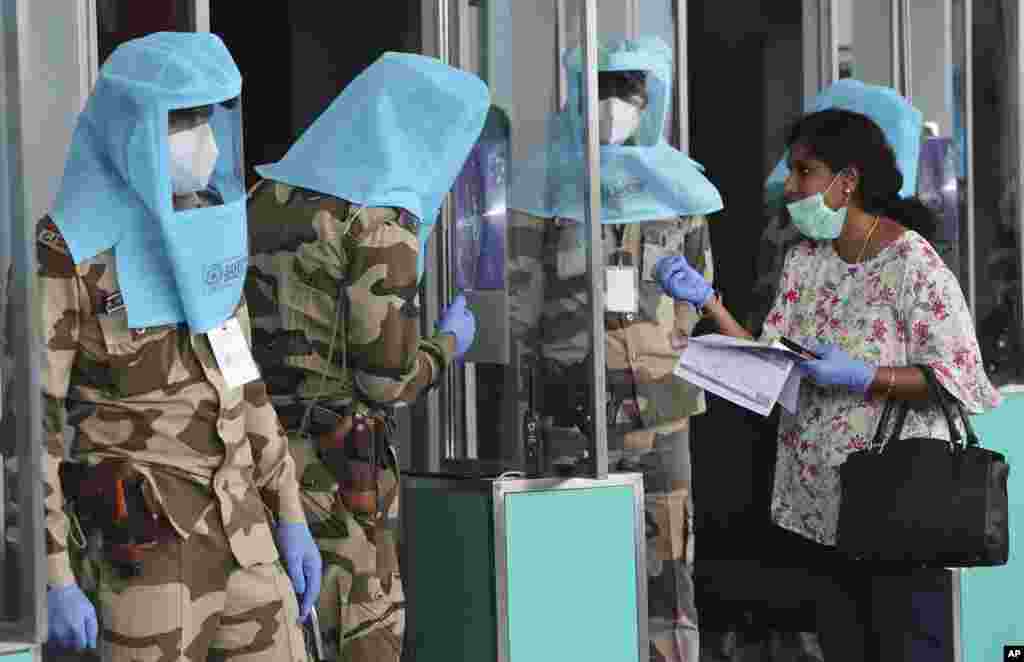 Indian security personnel wearing protective gear check the identity of a passenger through a glass inside the departure terminal at Kempegowda International Airport in Bengaluru.