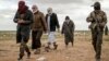 Men suspected of being Islamic State fighters walk next to a member of the Kurdish-led Syrian Democratic Forces (SDF) as they wait to be searched after leaving the IS group's last holdout, in Baghuz, Syria, Feb. 27, 2019.