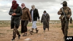 Muškarci, za koje se sumnja da su borci Islamske države, prolaze pored člana Sirijske demokratske snage (SDF) i idu na pretres prije nego napuste posljednje uporište Islamske države, Baghouz, Sirija, 27. februar 2019.