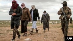 Men suspected of being an Islamic State (IS) group's fighter walk next to a member of the Kurdish-led Syrian Democratic Forces (SDF) as they wait to be searched after leaving the IS group's last holdout of Baghouz, Syria, Feb. 27, 2019.