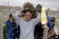 FILE - Holding a national Venezuelan flag, ousted Caracas Mayor Antonio Ledezma waves from inside El Dorado international airport, as he prepares for departure, in Bogota, Colombia, Nov. 17, 2017.