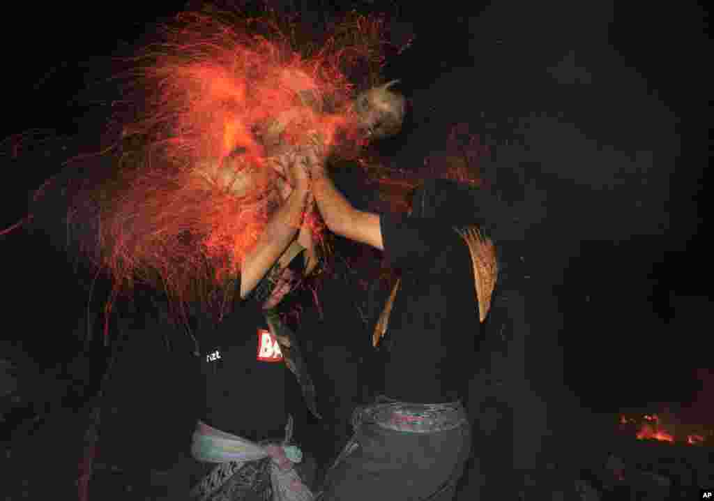 Balinese men lashing each other with burning coconut husks during 'Mesabatan Api', a sacred firefighting ritual at a Hindu temple in Bali, Indonesia.