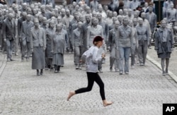 Una mujer cruza la calle frente a una manifestación llamada "1000 GESTALTEN", en la que miles de personas pintadas como figuras de barro avanzaban lenta y silenciosamente por las calles de Hamburgo para protestar contra la Cumbre del G20. Julio 7 de 2017.