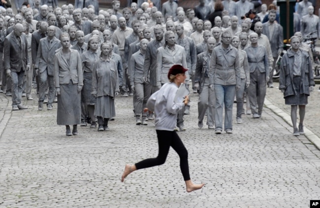 Una mujer cruza la calle frente a una manifestación llamada "1000 GESTALTEN", en la que miles de personas pintadas como figuras de barro avanzaban lenta y silenciosamente por las calles de Hamburgo para protestar contra la Cumbre del G20. Julio 7 de 2017.