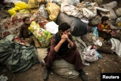 FILE - Afghan refugees sit on sacks filled with used plastic items to sell at their makeshift shelter in a slum on the outskirt of Lahore, Jan. 12, 2015.