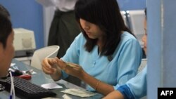 မွတ္တမ္း ႐ုပ္ပံု- ရန္ကုန္က ေငြလဲ ေကာင္တာမွာ ေငြစကၠဴကို စစ္ေဆးေနတဲ႔ ၀န္ထမ္းတဦး။ ဧၿပီ ၂၊ ၂၀၁၂။ (ဓာတ္ပံု Ye Aung Thu / AFP)