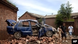 Chinese people walk past a flood-damaged vehicle sitting on the bricks at a village in Fangshan district of Beijing, China, July 23, 2012. 
