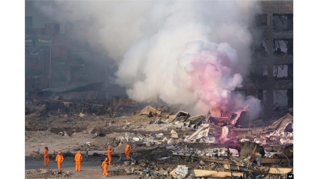 Fire fighters in protective gear watch partially pink smoke continue to billow after an explosion at a warehouse in northeastern China's Tianjin municipality, Aug. 13, 2015.