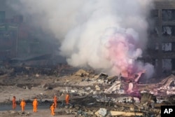 Fire fighters in protective gear watch partially pink smoke continue to billow after an explosion at a warehouse in northeastern China's Tianjin municipality, Aug. 13, 2015.