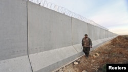 A Kurdish People's Protection Units (YPG) fighter walks near a wall, which activists said was put up by Turkish authorities, on the Syria-Turkish border in the western countryside of Ras al-Ain, Syria, Jan. 29, 2016.