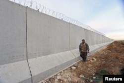 FILE - A Kurdish People's Protection Units (YPG) fighter walks near a wall, which activists said was put up by Turkish authorities, on the Syria-Turkish border in the western countryside of Ras al-Ain, Syria, Jan. 29, 2016.