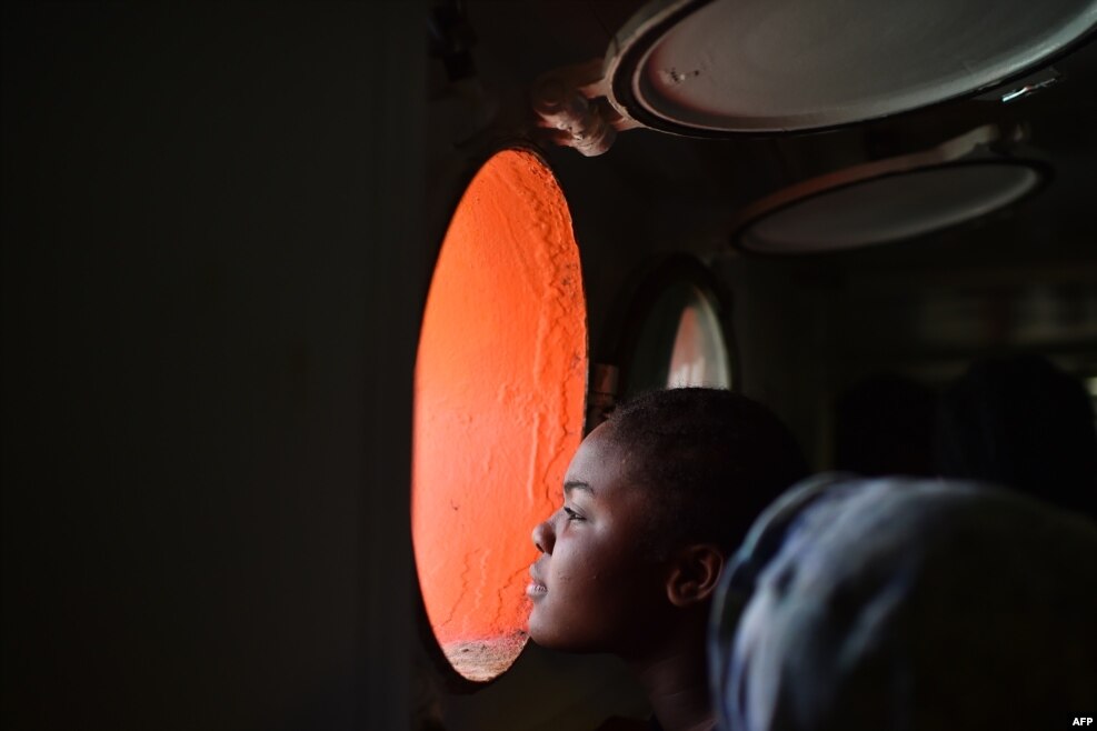 A woman looks through a window of rescue ship &quot;Aquarius&quot; as more the 380 migrants arrive in the port of Cagliari, Sardinia on May 26, 2016 two days after being rescued near the Libyan coasts.