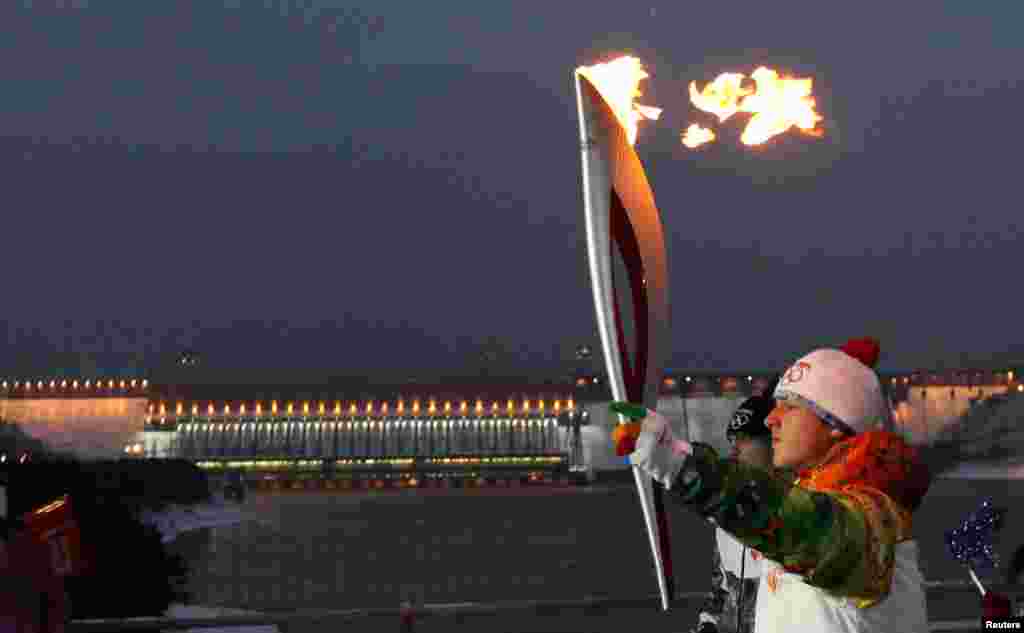 A runner carries the Sochi 2014 Winter Olympic torch along a bridge across Yenisei River near the Krasnoyarsk hydro electric power station near the town of Divnogorsk outside Krasnoyarsk, Russia.