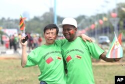 An unidentfied Chinese national and a Zimbabwean man hug while welcoming Chinese President Xi Jinping upon his arrival in Harare, Zimbabwe, Tuesday, Dec. 1. 2015.