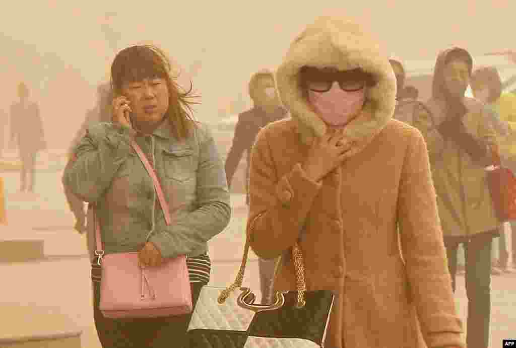 Residents walk on a street during a sandstorm in Hami, northwestern China&#39;as Xinjiang Uyghur autonomous region. Hami issued an &quot;orange alert&quot; for a sandstorm, warning residents to reduce outdoor activities and avoid dangerous jobs.