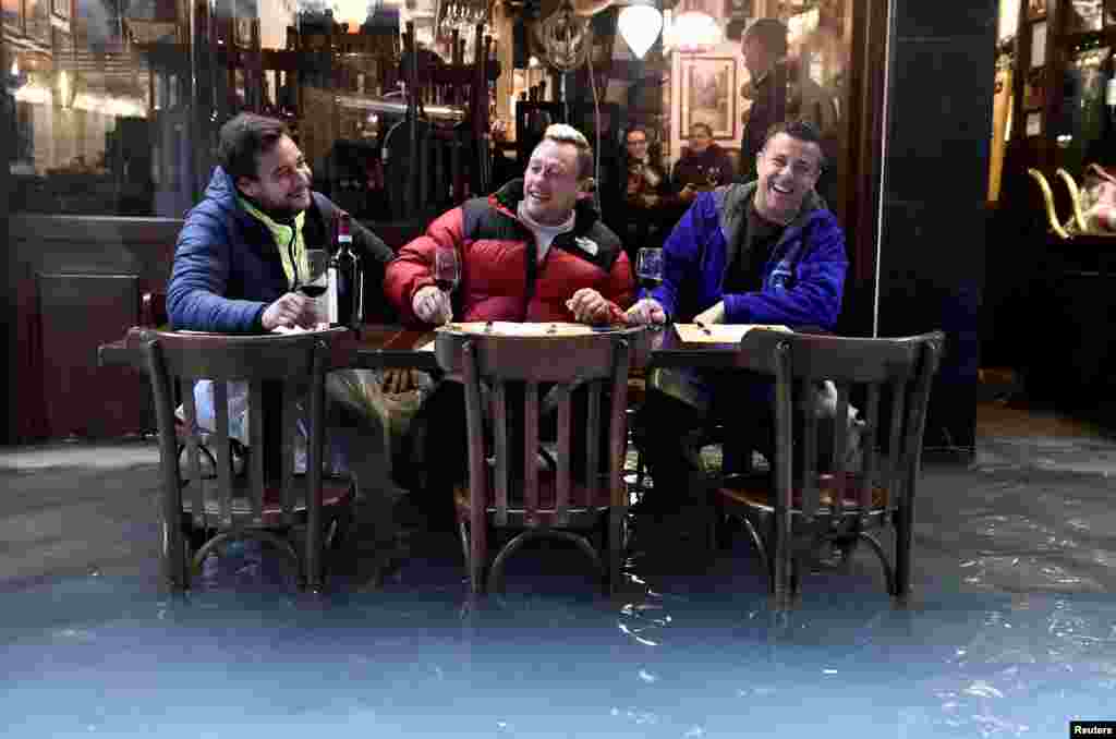 Men have a glass of wine at a flooded street in Venice, Italy.