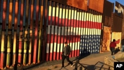 FILE - People pass graffiti along the border structure in Tijuana, Mexico, Jan. 25, 2017.
