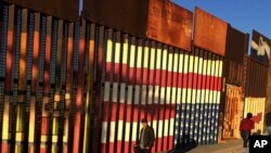 People pass graffiti along the border structure in Tijuana, Mexico, Jan. 25, 2017.