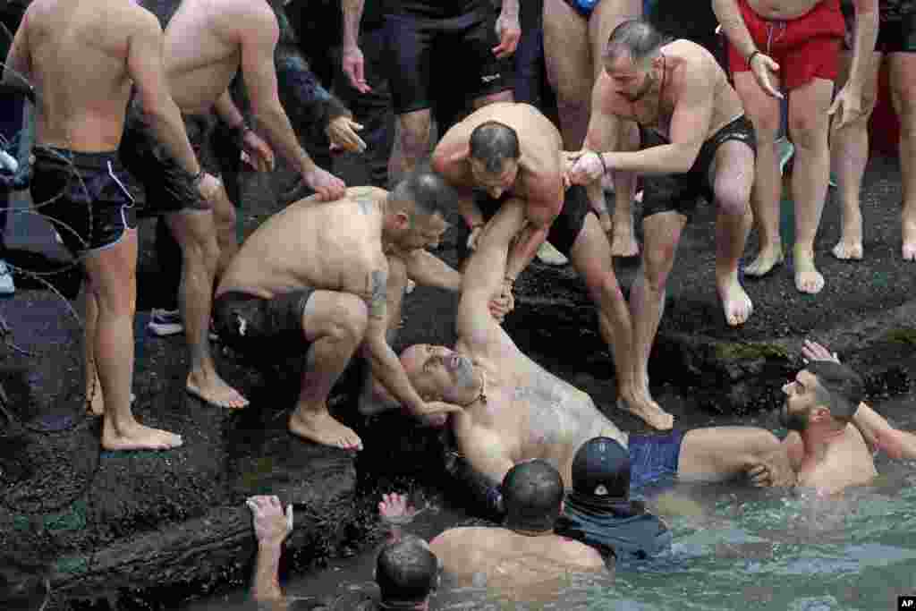 Swimmers pull a Greek Orthodox faithful who lost consciousness, out of the water as he swam with others to retrieve a wooden crucifix during the Epiphany ceremony in Istanbul, Turkey. 