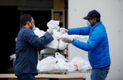 Hazim Macky mengambil makan berbuka puasa dari Mohamed Saleem yang disiapkan untuk masyarakat di luar Asosiasi Muslim Puget Sound pada hari pertama Ramadan di tengah wabah corona di Redmond, Washington, AS, 24 April 2020. (Foto: Reuters)