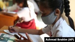 Seorang siswi mengenakan masker untuk mencegah penularan virus corona sedang belajar daring dengan memanfaatkan akses wifi gratis di kantor Kelurahan Jatirahayu, Bekasi, 27 Juli 2020. (Foto: AP) 