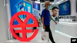 A visitor passes by a logo for the e-CNY, a digital version of the Chinese Yuan, displayed during a trade fair in Beijing, China, Sunday, Sept. 5, 2021. (AP Photo/Ng Han Guan)