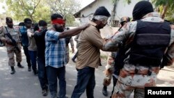 FILE - Paramilitary soldiers escort blindfolded men, who were detained during a raid on the Muttahida Qaumi Movement political party headquarters, after presenting them before an anti-terrorism court in Karachi, March 12, 2015.