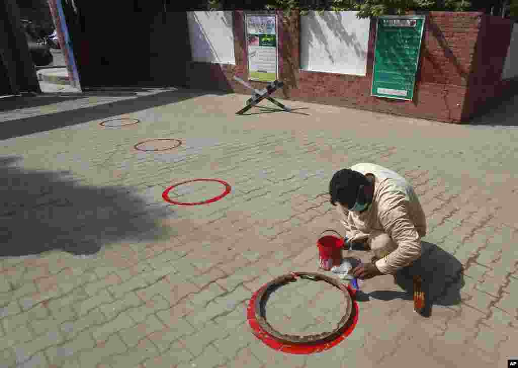 A worker paints circles for social distance at an entry gate of a school as preparation for reopening of educational institutions that were closed in March are finalized, in Lahore, Pakistan.